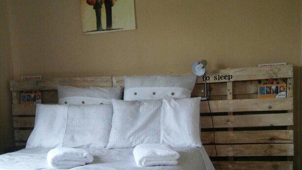 Una cama bien hecha con sábanas blancas y dos toallas dobladas, un cabecero de madera con un cartel que dice 'para dormir' y un cuadro colgado en la pared.
