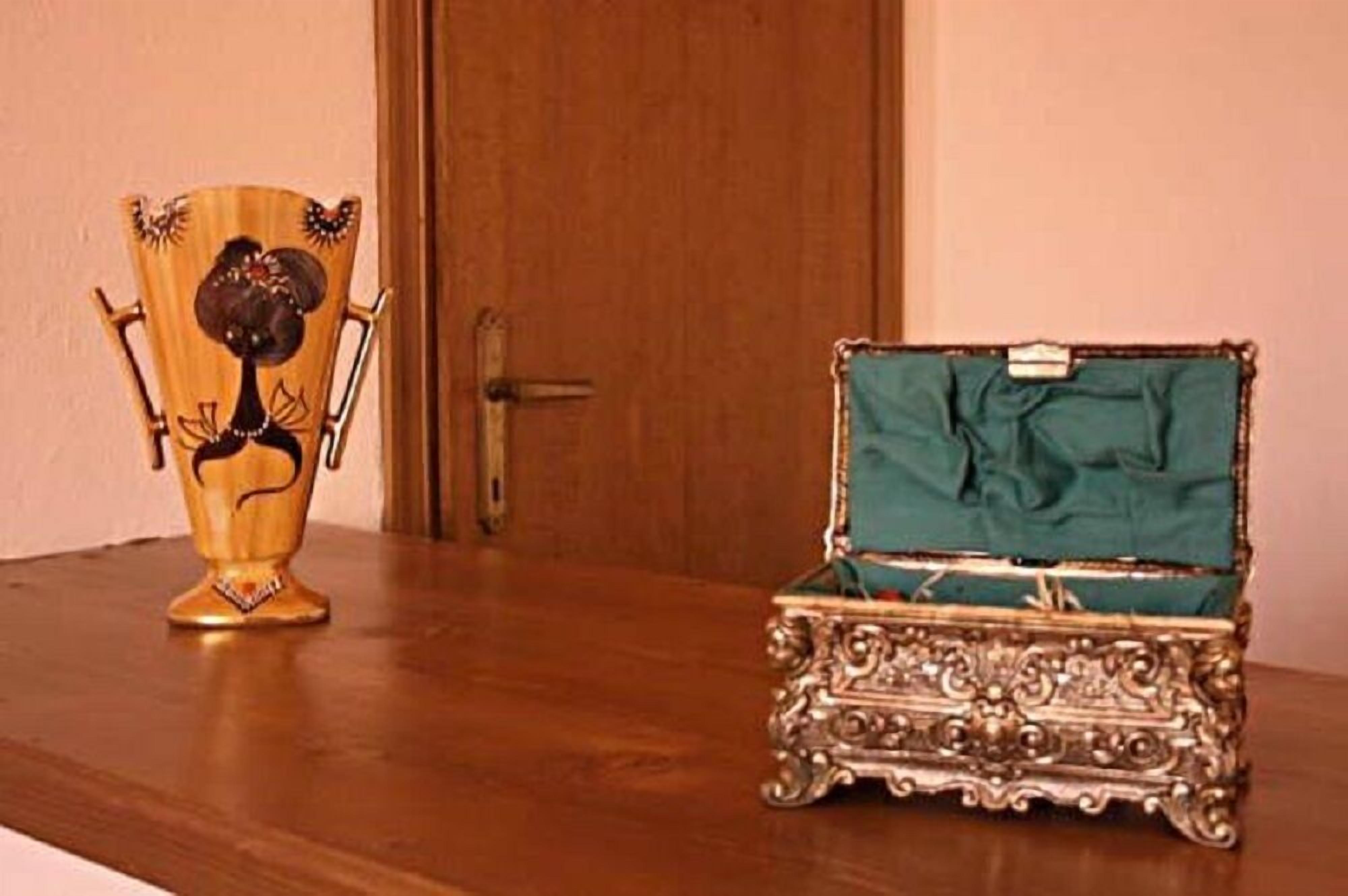 Een houten tafel met een decoratieve vaas en een open sieradendoosje met een groene binnenkant.