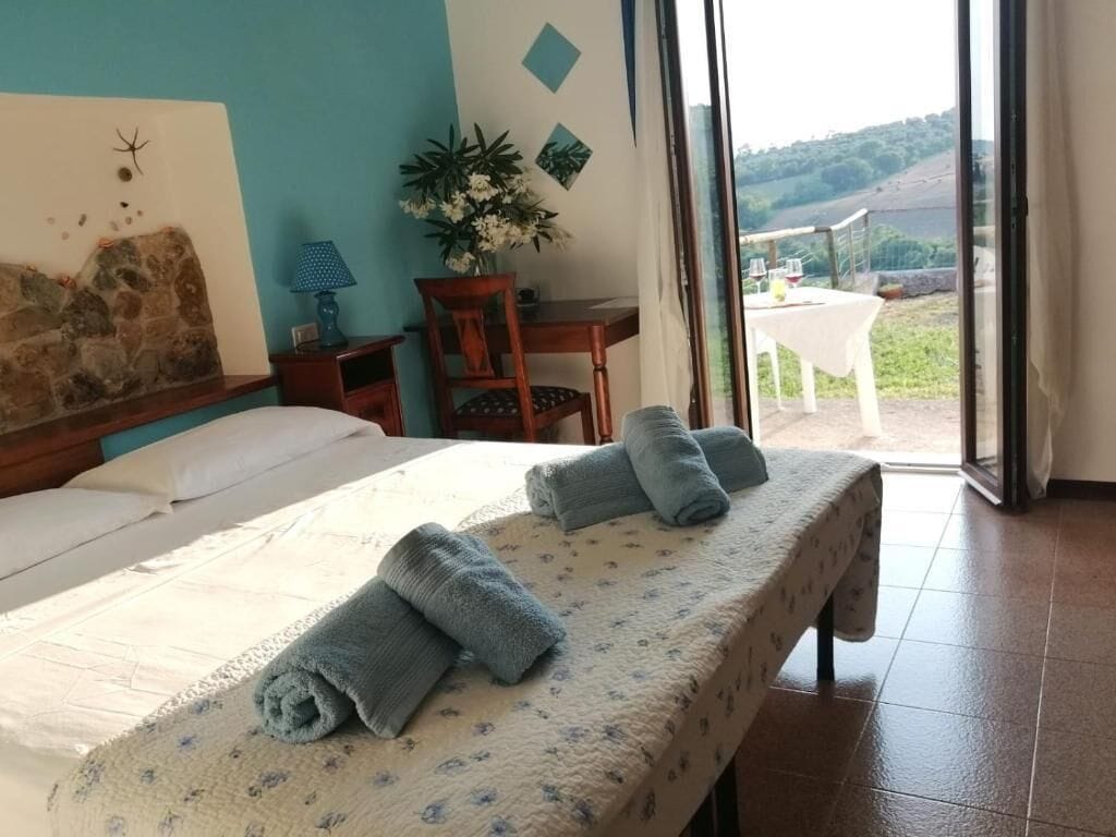 Ein Hotelzimmer mit Bett, Tisch, Stuhl, Lampe und Blick ins Freie.