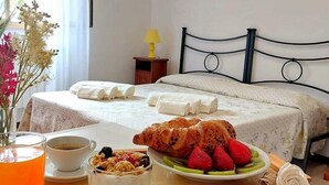 Une chambre d’hôtel avec un lit parfaitement fait, un plateau de petit-déjeuner comprenant des croissants, des fraises et du yaourt, et une tasse de café.