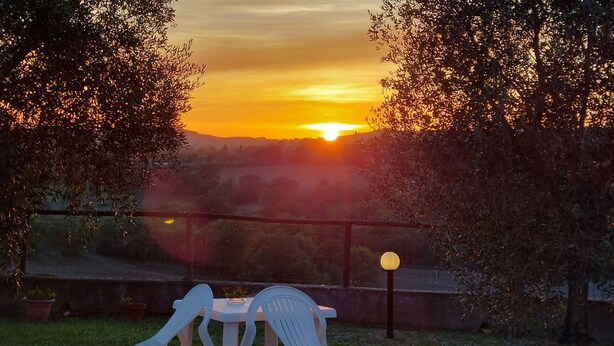 Une vue sur le coucher de soleil depuis un balcon, avec une table et des chaises, le tout entouré d’arbres.