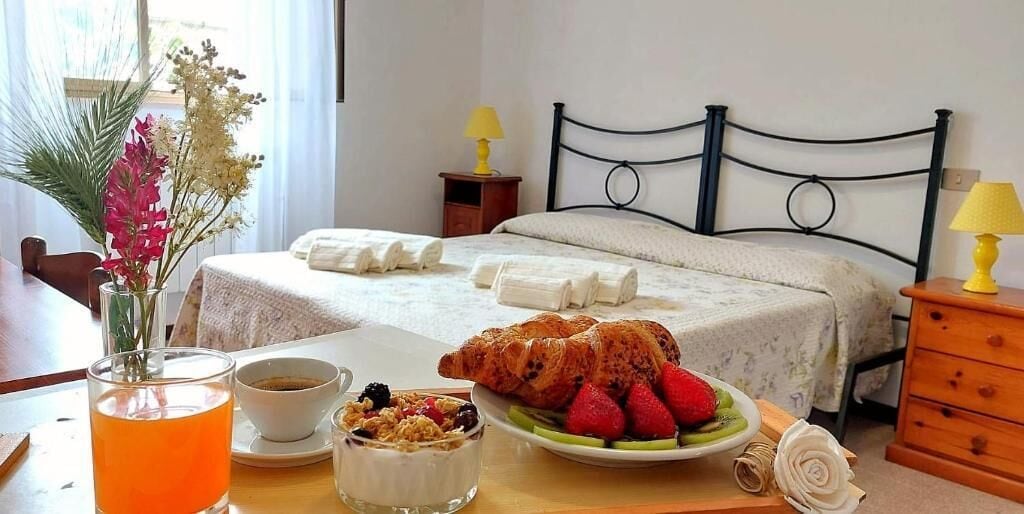 Una habitación de hotel con dos camas, una mesa de comedor con desayuno y un jarrón de flores.