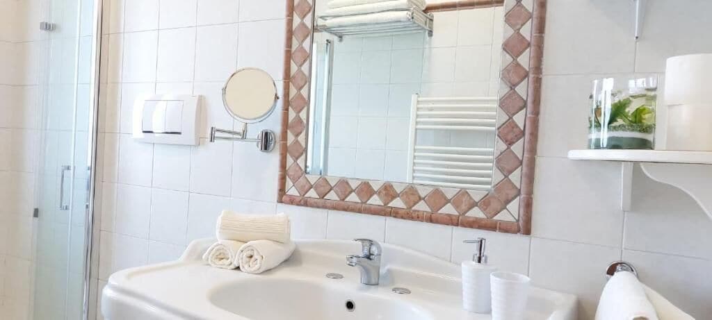 A bathroom with a sink, mirror, towel rack, and a glass shelf.