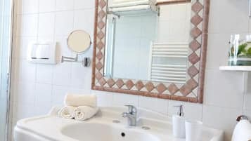 Ein Badezimmer mit Waschbecken, Spiegel, Handtuchhalter und einer Glasablage.