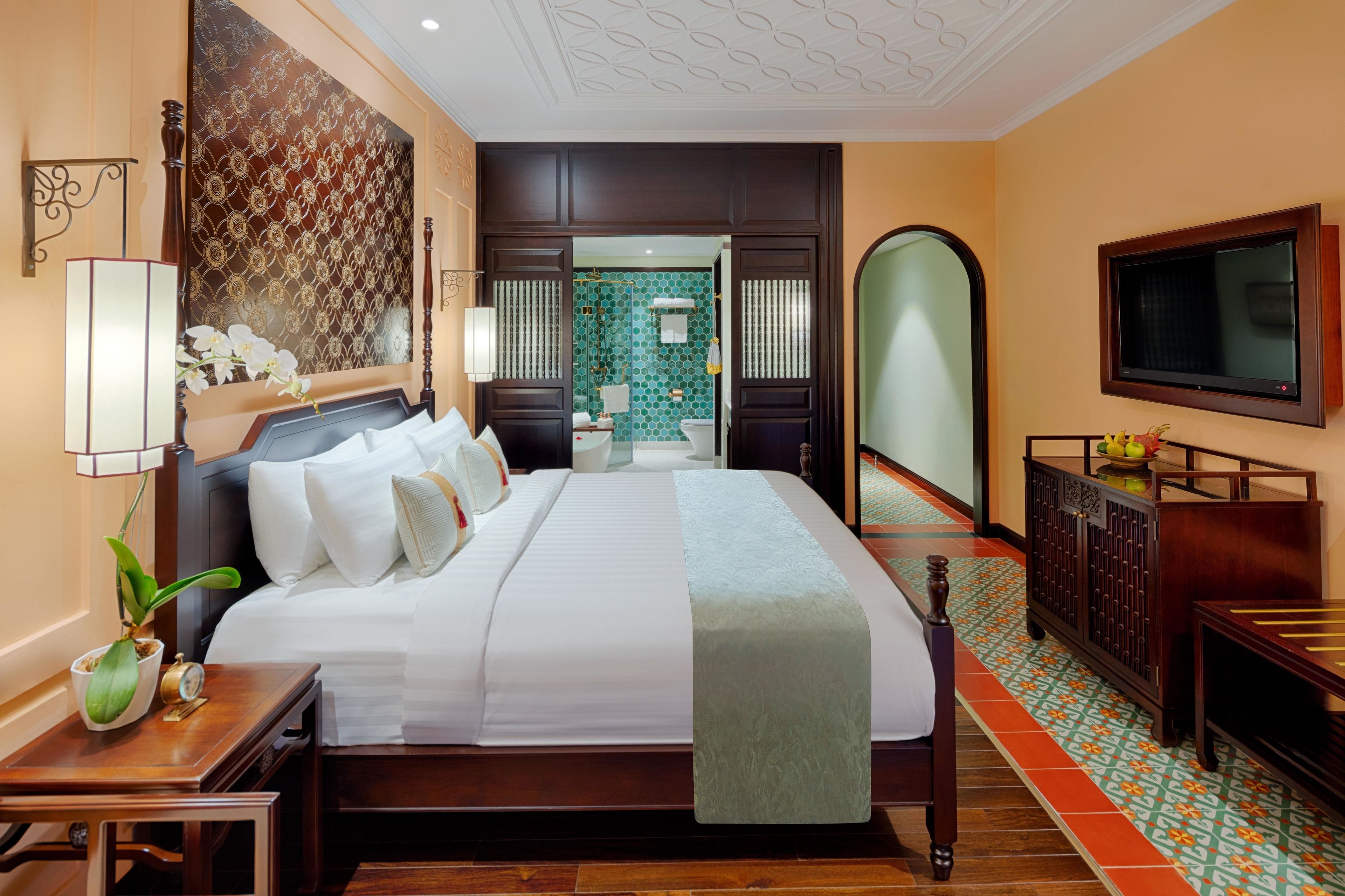 A spacious hotel room with a large bed, a television, a wooden cabinet, and a decorative wall panel.