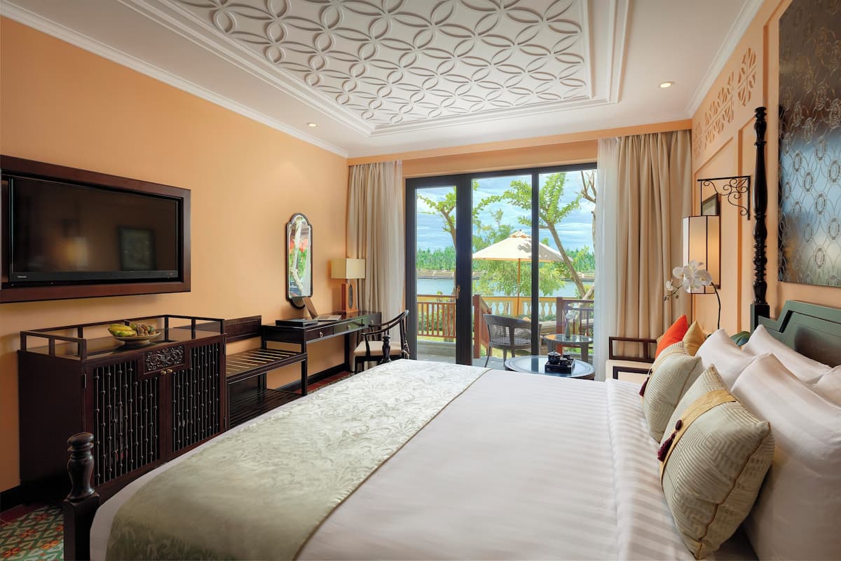 A hotel room with a large bed, a desk, a television, and a balcony with a view of the outdoors.