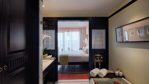 A modern hotel room with a large bed, a bathroom with a bathtub, and a view of the city. - Little Riverside. A Luxury Hotel & Spa (Da Nang)