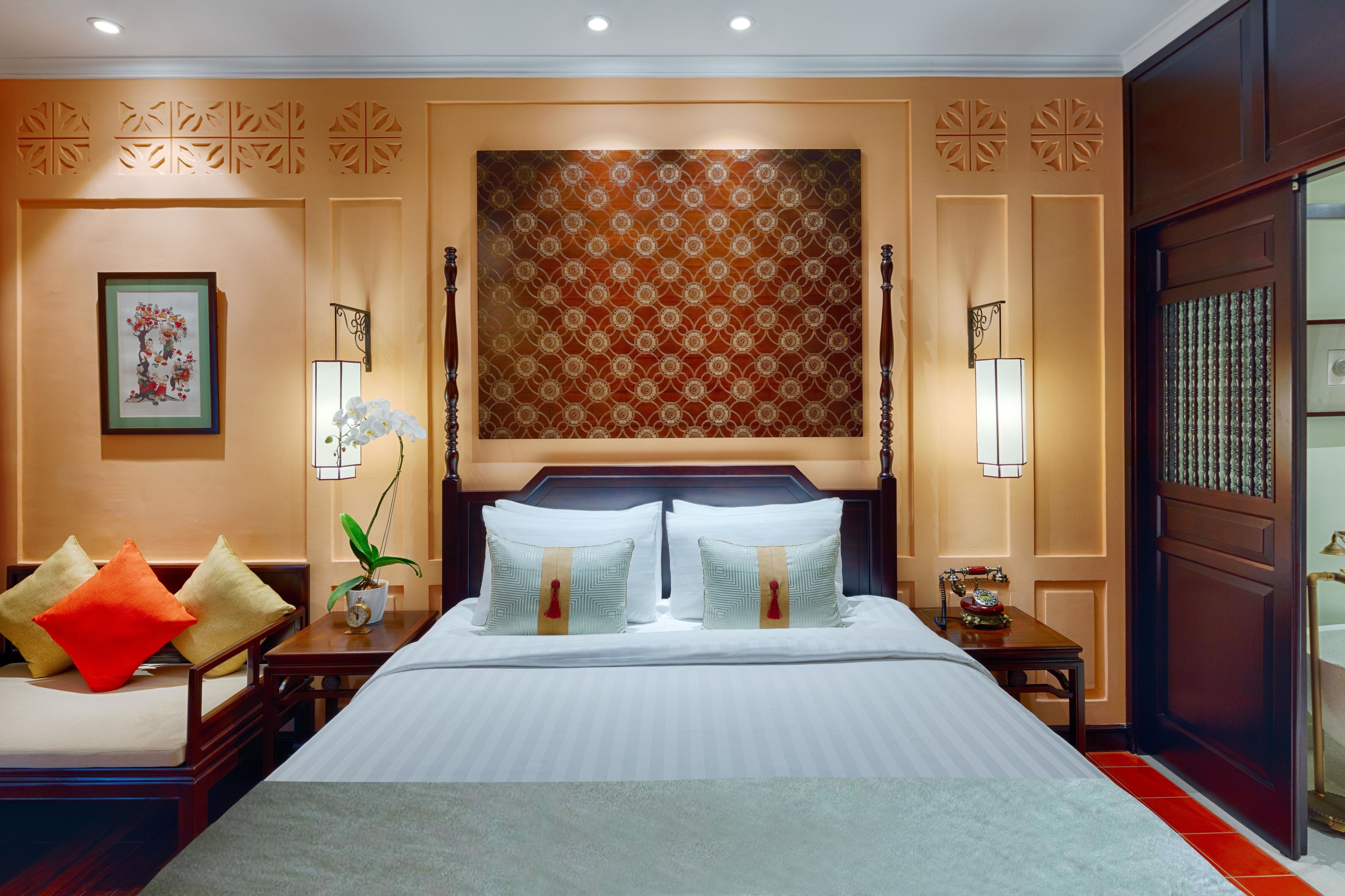 Une chambre d’hôtel avec un grand lit, deux tables de chevet, une petite table d’appoint, un panneau décoratif mural et une œuvre d’art encadrée.