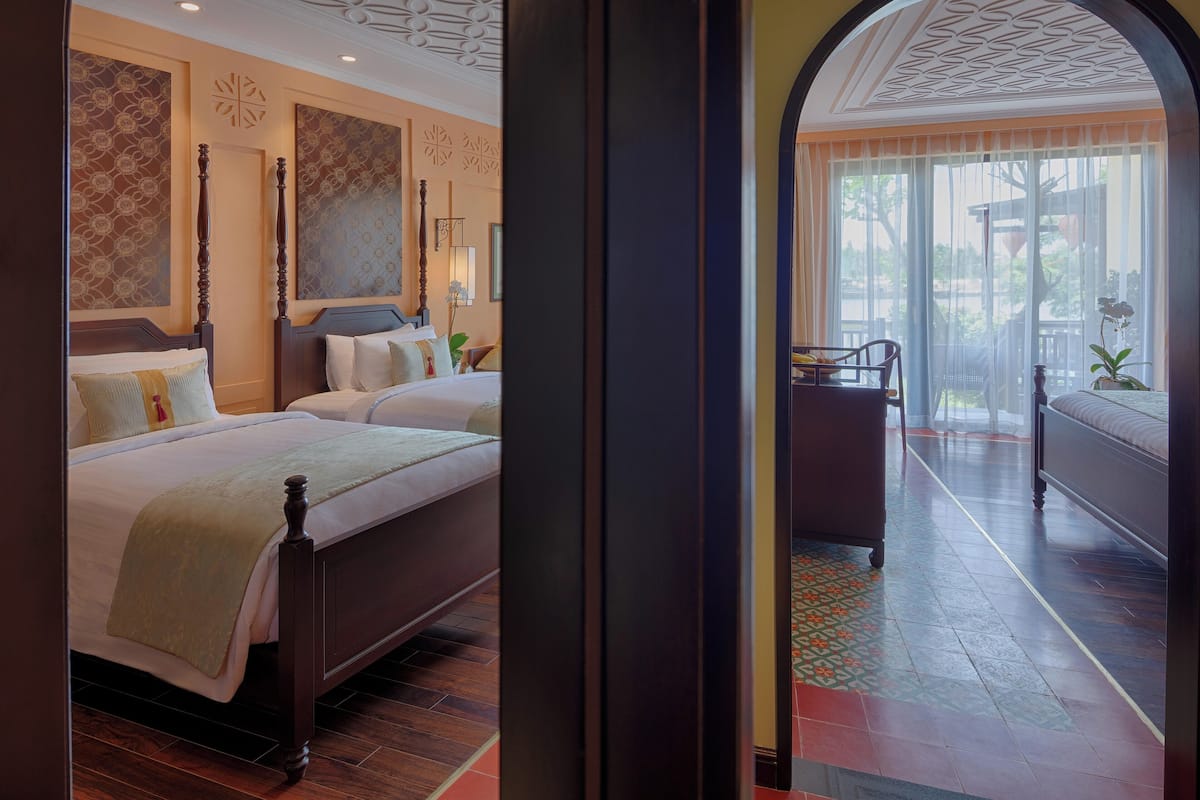 A hotel room with two beds, a balcony, and a view of the outdoors.
