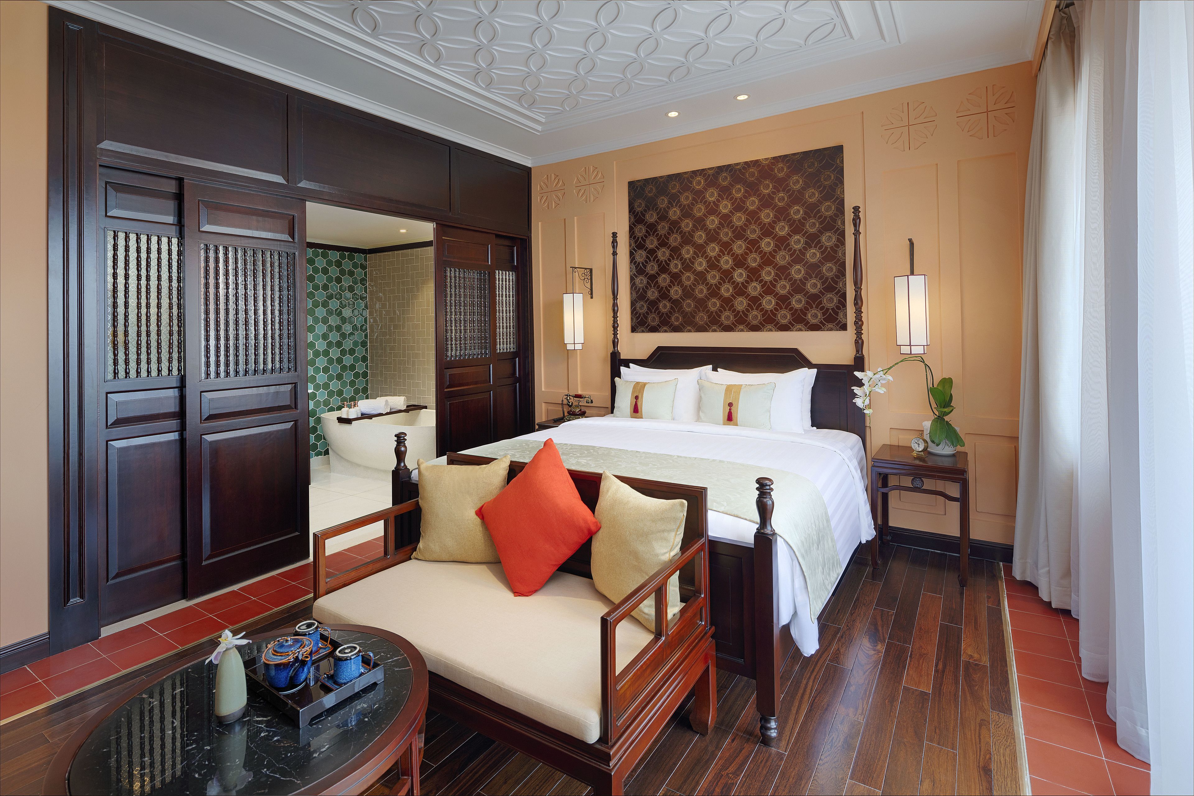 Une chambre d’hôtel avec un grand lit, un canapé, une petite table agrémentée d’objets décoratifs et un miroir.