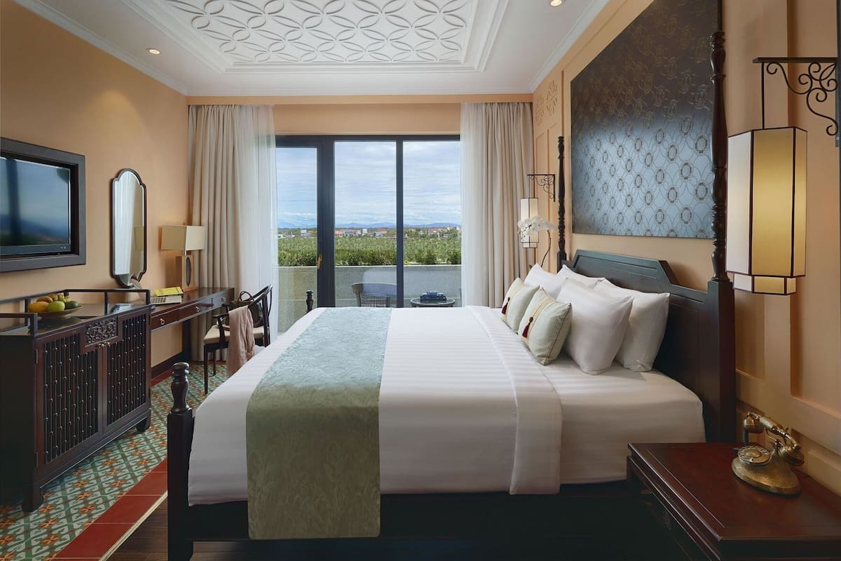 A hotel room with a large bed, a TV, a desk with a chair, a balcony with a view, and a decorative wall.