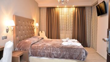 A hotel room with a large bed, a headboard, two wall-mounted lamps, a flat-screen TV, and a large window with curtains.