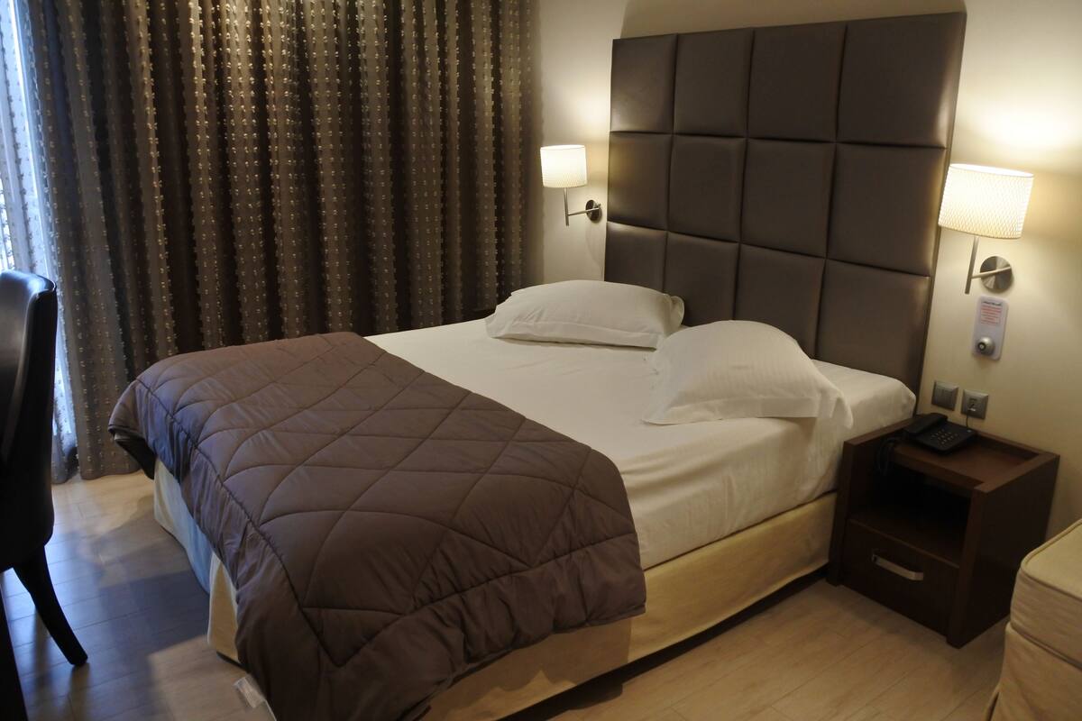 A hotel room with a large bed, two bedside lamps, a nightstand with a phone, and a chair.