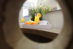 A breakfast tray with fruits and a glass of orange juice, a white cup, and a tissue box on a wooden surface. - Konaki Hotel & SPA (Aristotelis)