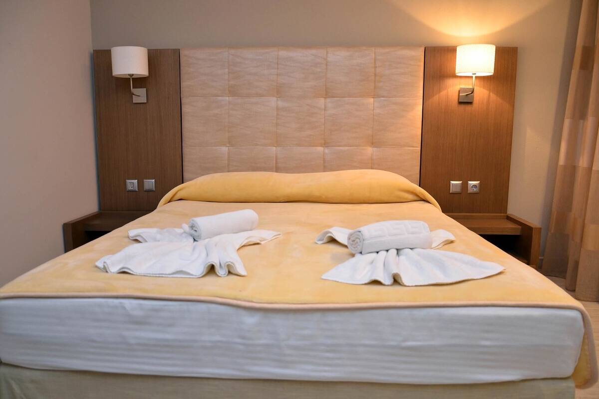 A hotel room with a bed, two bedside tables, and two wall-mounted lamps.