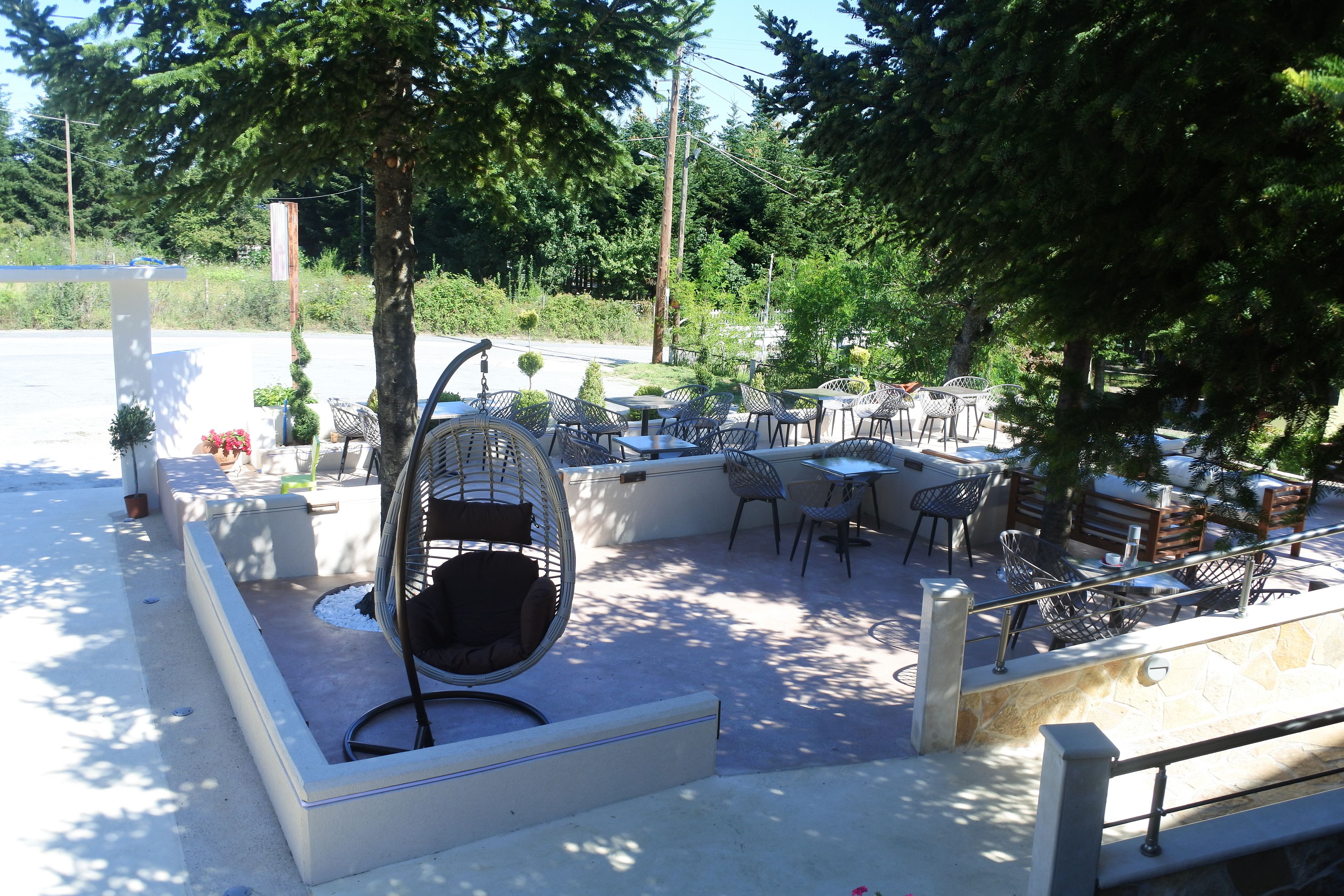 An outdoor patio area with seating arrangements, including chairs and tables, surrounded by trees and greenery.