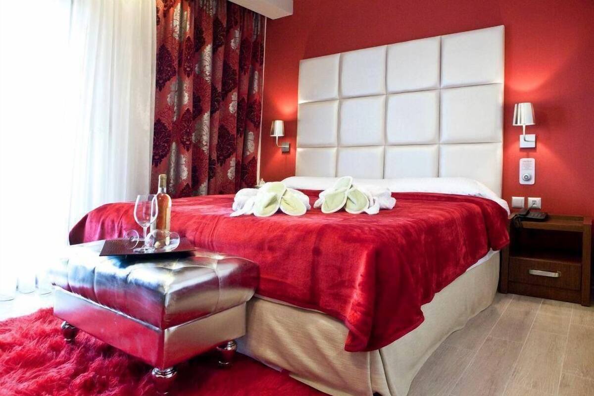 A hotel room with a large bed, a red upholstered bench, and a red carpet.