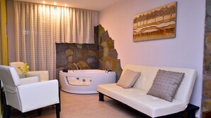 A spa room with a white sofa, a white chair, a stone wall, a painting, and a bathtub. - Konaki Hotel & SPA (Aristotelis)