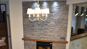 A modern interior with a stone wall, a fireplace, and a chandelier. - Konaki Hotel & SPA (Aristotelis)