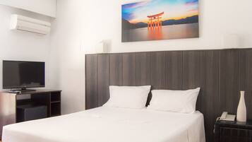 A hotel room with a bed, a TV, a painting of a sunset, and a wooden headboard.