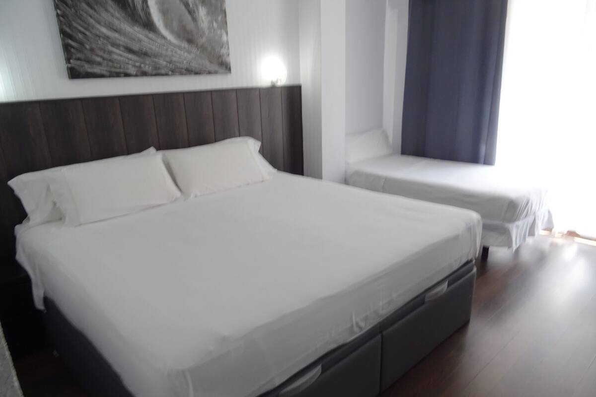 Ein modernes Hotelzimmer mit einem großen Bett, einem kleineren Bett und einem Nachttisch.