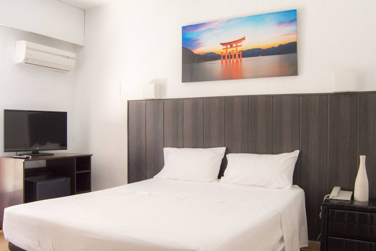 Ein Hotelzimmer mit einem Bett, einem Fernseher, einem Sonnenuntergangsbild und einem Holzkopfteil.