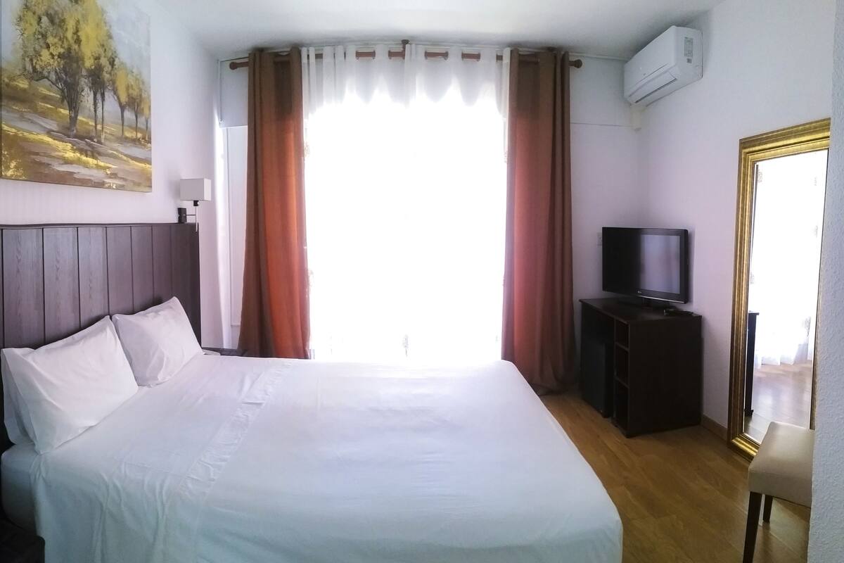 Ein Hotelzimmer mit Bett, Fernseher auf einem Schrank, einem Bild an der Wand und einer Klimaanlage.