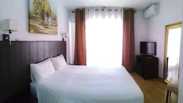 Habitación de hotel con cama, televisor sobre un mueble, un cuadro en la pared y un equipo de aire acondicionado.