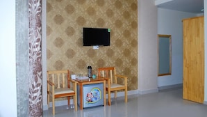 A room with a patterned wallpaper, a flat-screen TV mounted on the wall, a small table with chairs, and a refrigerator with a cartoon character on it.