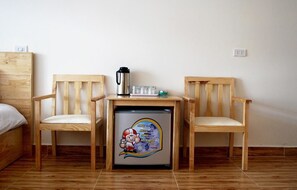 A small room with a bed, two wooden chairs, a table with a coffee maker, and a refrigerator with a sticker.