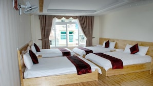 A hotel room with four single beds, a large window with curtains, and a ceiling fan.