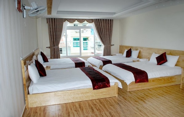 A hotel room with four single beds, a large window with curtains, and a ceiling fan.