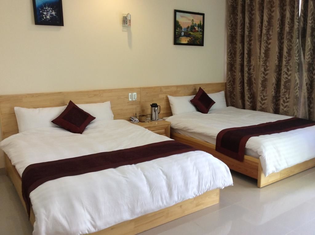 A hotel room with two single beds, each with a wooden headboard, white bedding, and a red throw blanket. There is a nightstand with a lamp and a coffee maker on each bed.