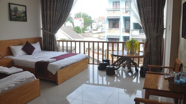 A hotel room with a balcony, a bed, a small table, and a view of the cityscape.