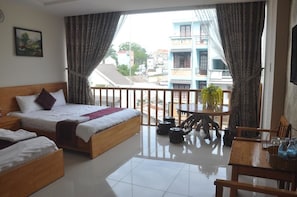A hotel room with a balcony, a bed, a small table, and a view of the cityscape.