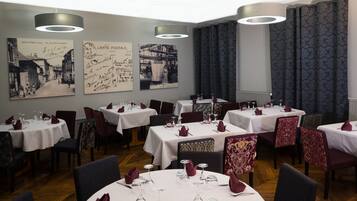 Un restaurant avec des tables rondes dressées pour le repas, agrémentées de nappes blanches et de serviettes rouges.