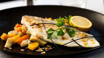 A dish of fish with almonds and orange vegetables on a black plate.