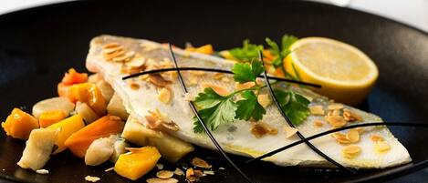 A dish of fish with almonds and orange vegetables on a black plate.