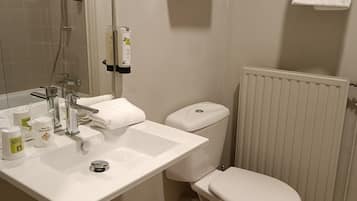 A modern bathroom with a white sink, toilet, and shower. There are toiletries on the sink and a towel rack above the toilet.