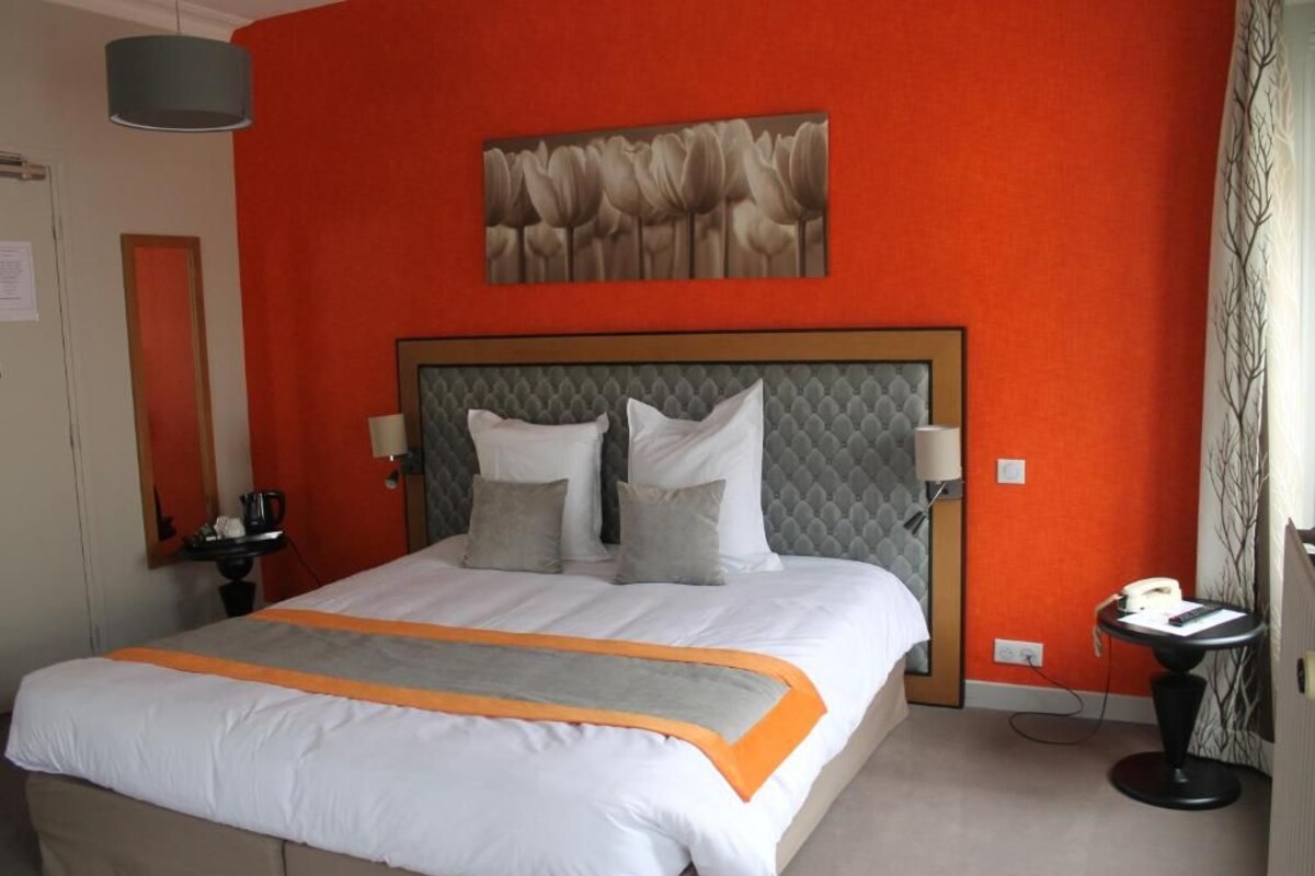 Una habitación de hotel con una cama grande, un cabecero gris y una pared de acento roja.