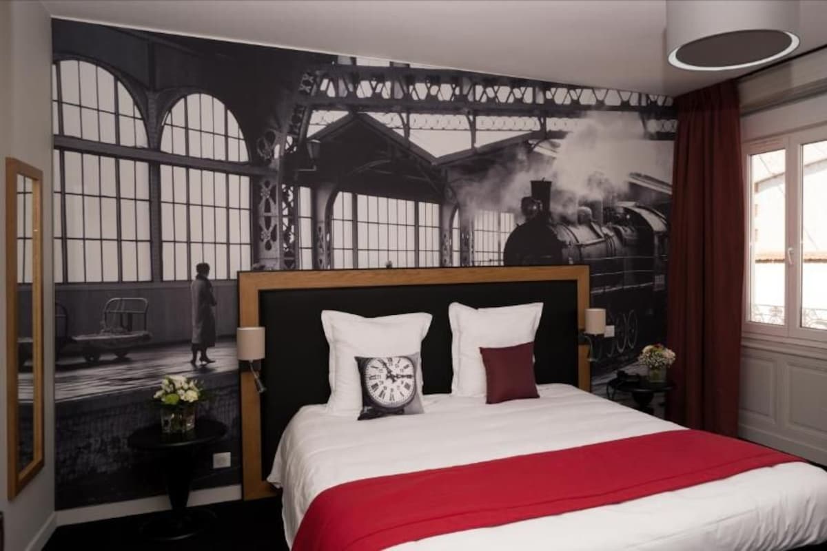A hotel room with a large bed, a clock, and a mural of a train station.