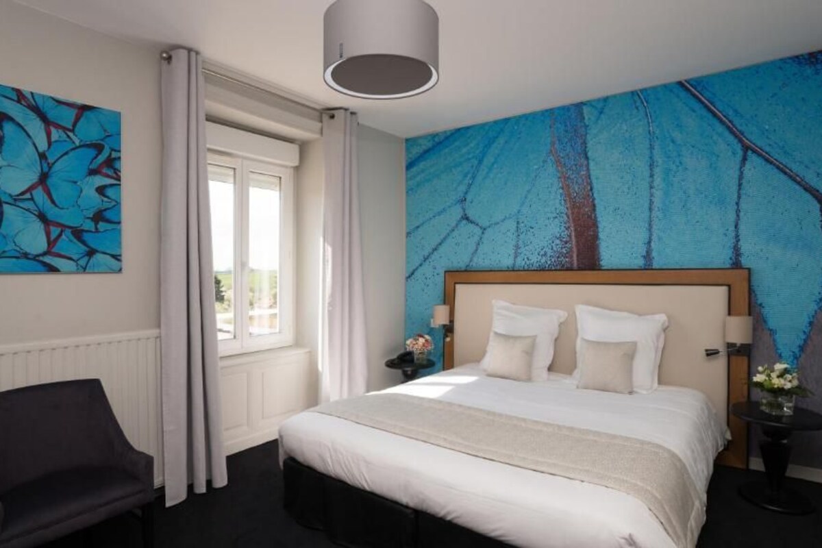 Un dormitorio con una cama grande, una silla, un ventanal con cortinas y un cuadro en la pared.