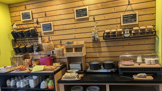 Una barra de café con paneles de madera, cestas colgantes, frascos y una exhibición de productos de panadería.