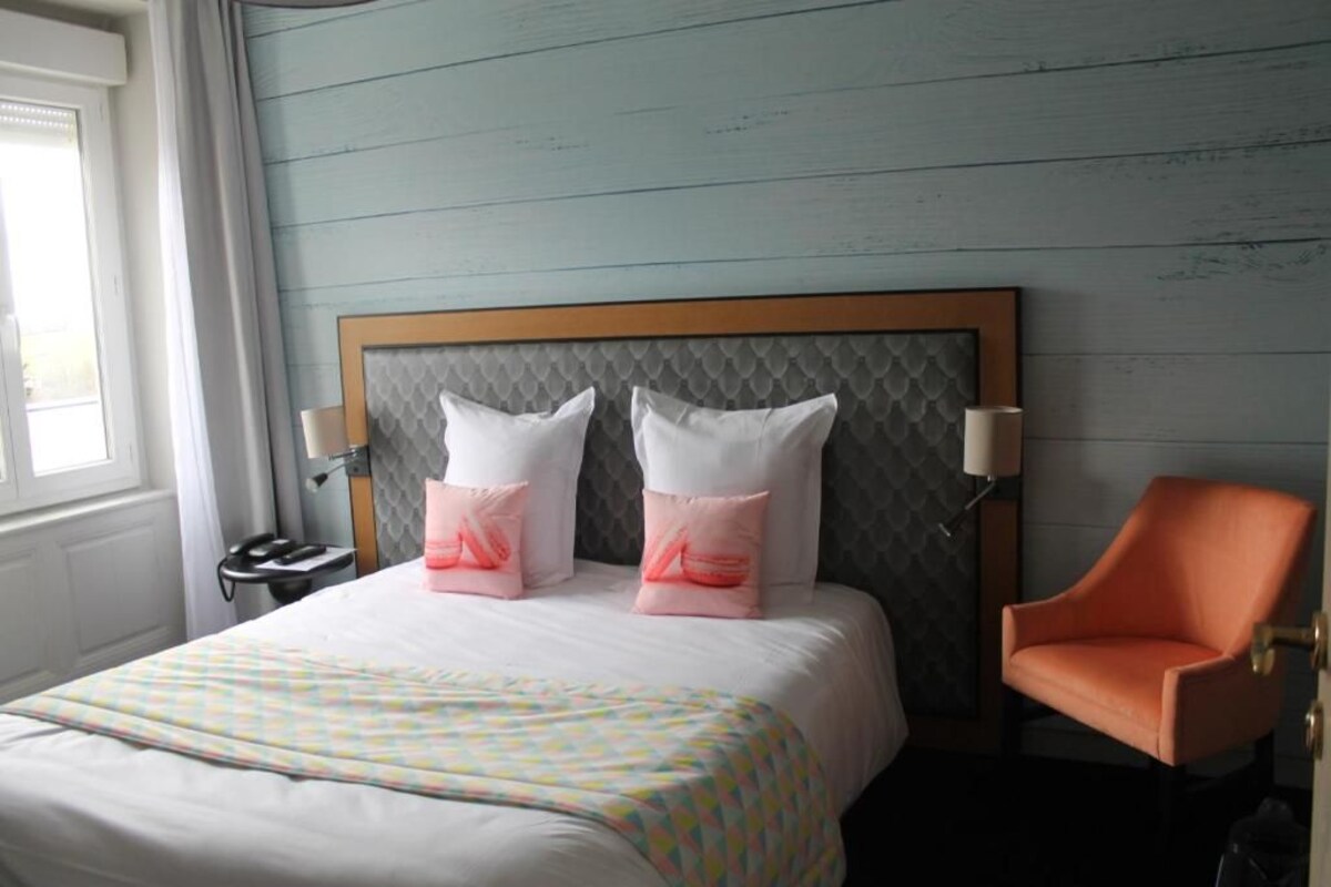 Une chambre d’hôtel avec un lit, deux oreillers, une chaise et une table de chevet avec une lampe.