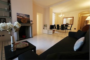 Una sala de estar con chimenea, un comedor con candelabro y un sofá negro.