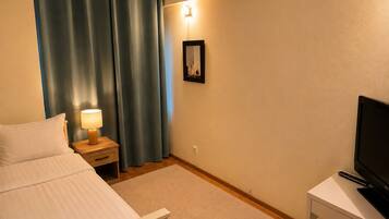 Una habitación de hotel con una cama, una mesita de noche con una lámpara, un televisor en un mueble bajo y un cuadro en la pared.
