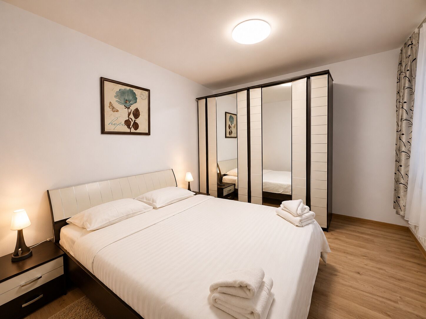 Een hotelkamer met een bed, nachtkastjes, een spiegel en een kledingkast.