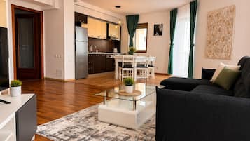Una sala de estar moderna con un sofá negro, una mesa de centro de vidrio y un comedor con una mesa y sillas blancas.