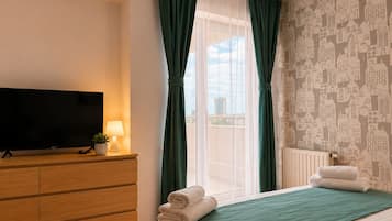 A hotel room with a bed, a TV on a wooden dresser, a window with green curtains, and a patterned wall.