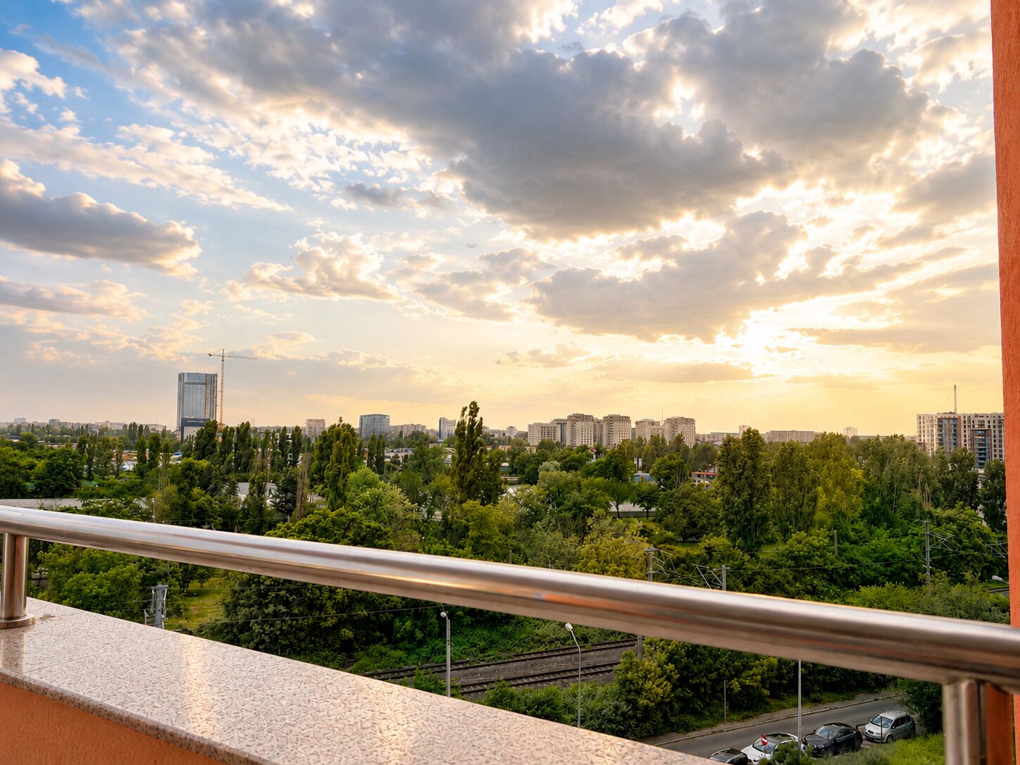A balcony with a metal railing overlooking a cityscape with buildings and greenery.